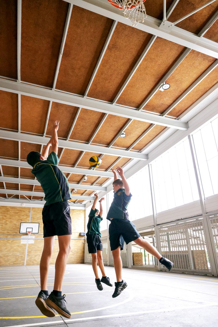 Three male students jump and reach for a basketball.