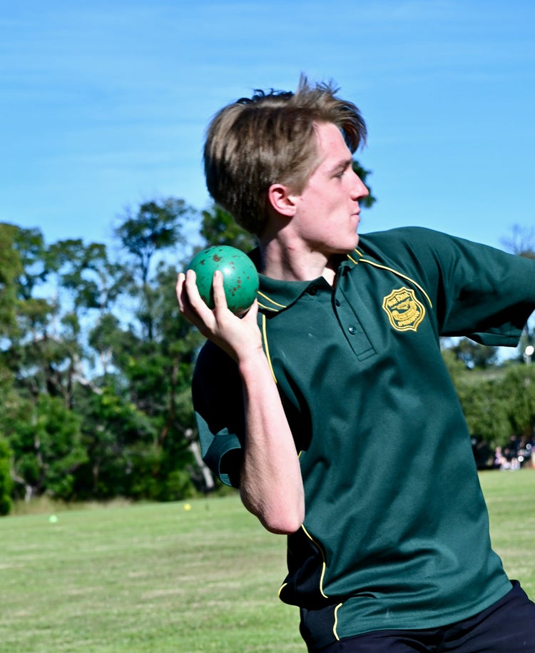 A male student in the Springwood High School green PE polo shirt holds a shot put ready to throw.