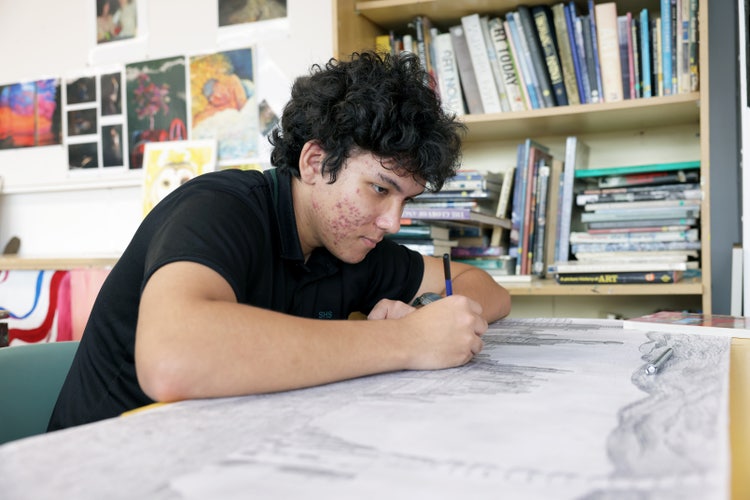 A male student draws on a large sheet of paper.