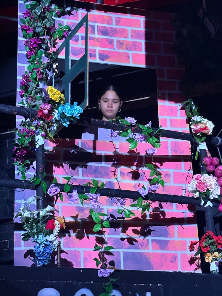 A student performer looks from a window covered in flowers.