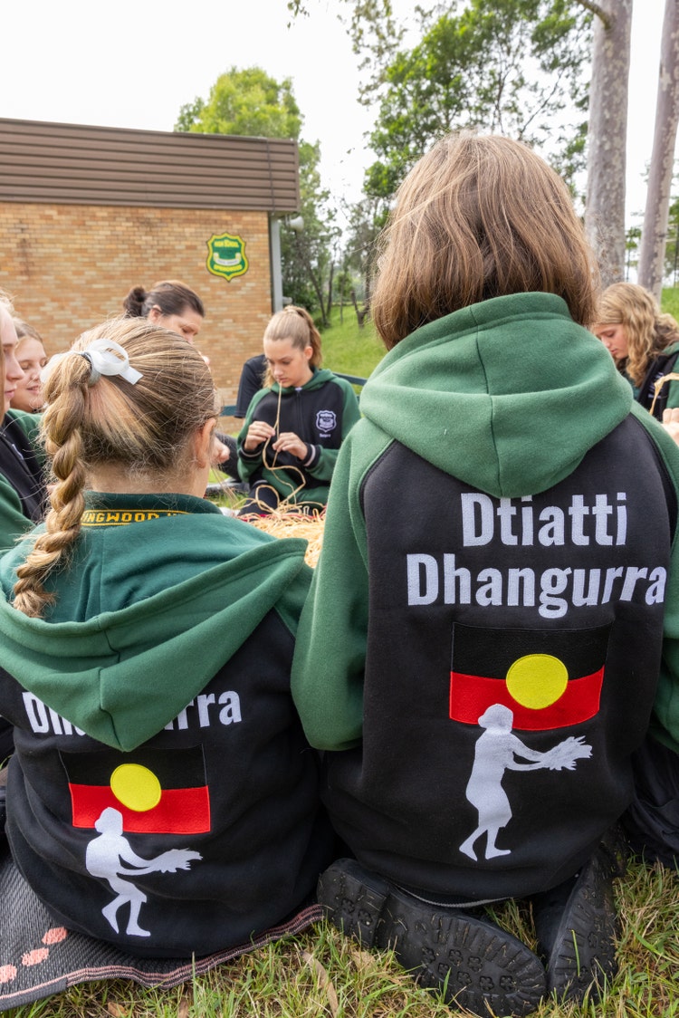 Students sit facing each other while weaving. The back of the students' jumpers is shown to say Dtiatti Dhangurra.